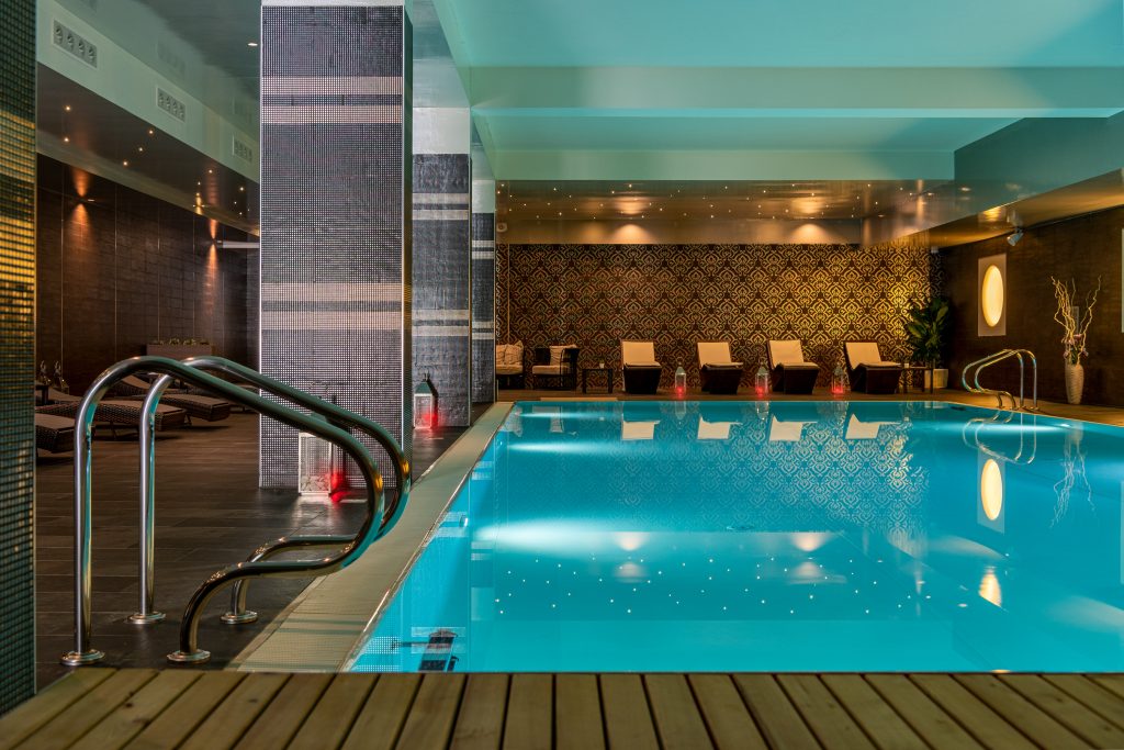 Piscina interna elegante con lettini e illuminazione soffusa.