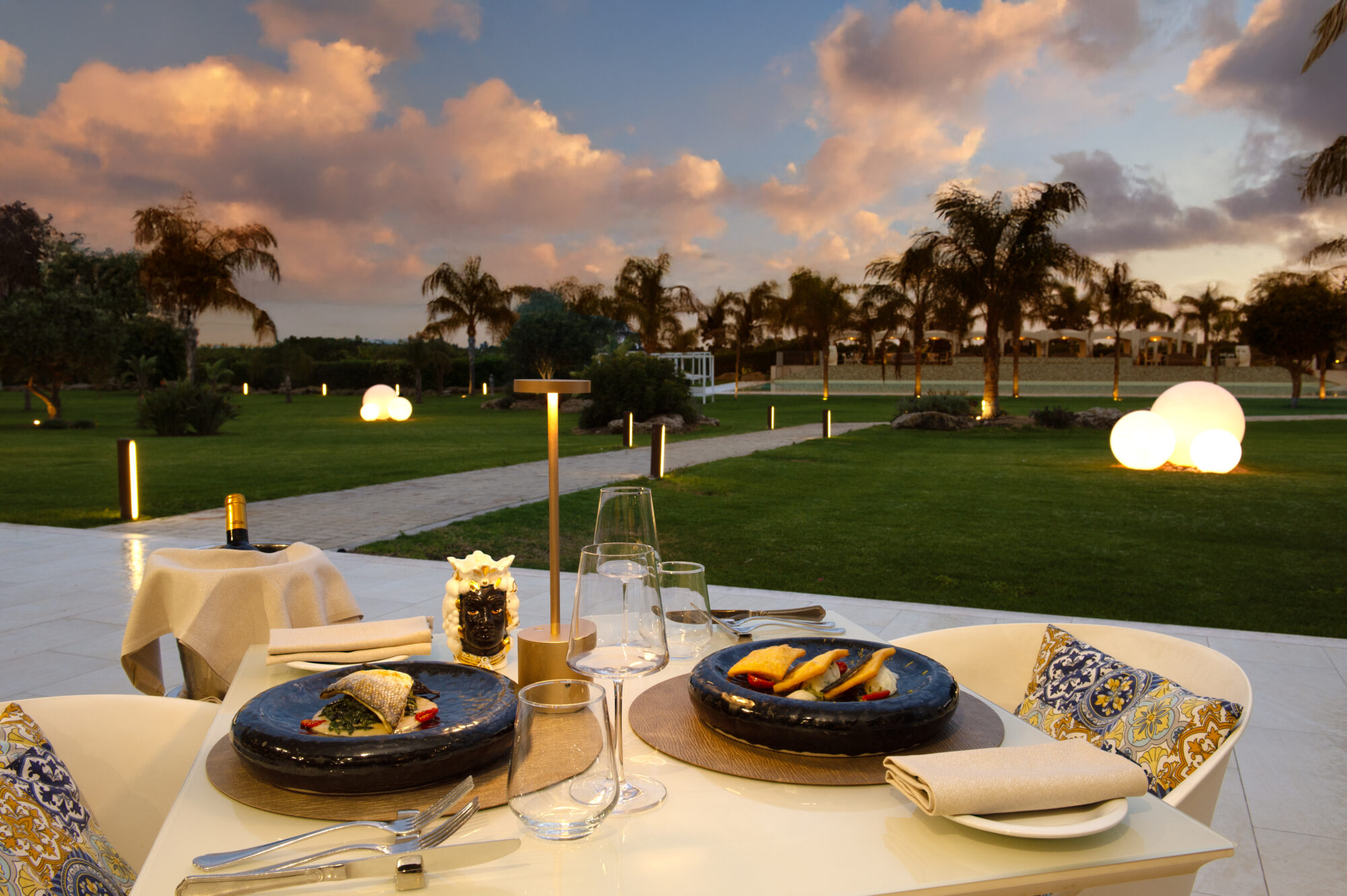 Cena elegante all'aperto al tramonto con vista su un giardino illuminato.