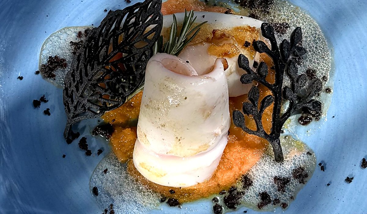 Un piatto gourmet con una preparazione artistica su un piatto blu.